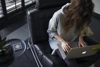 穿着蓝色长袖上衣的女人坐在黑色皮革椅子上，膝盖上放着银色的MacBook